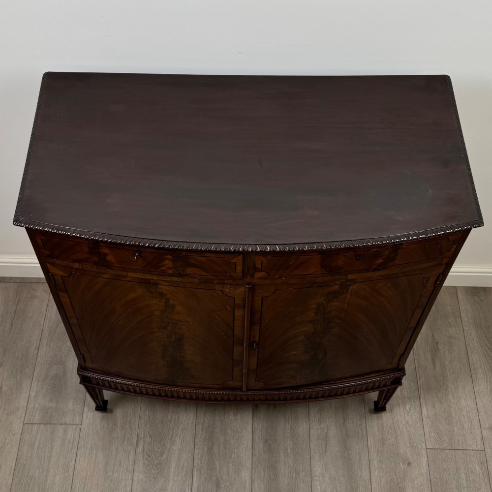 An 18th-century Georgian mahogany cupboard featuring flame veneer panelled doors, upper drawer section, a fluted apron, and tapered legs. View X