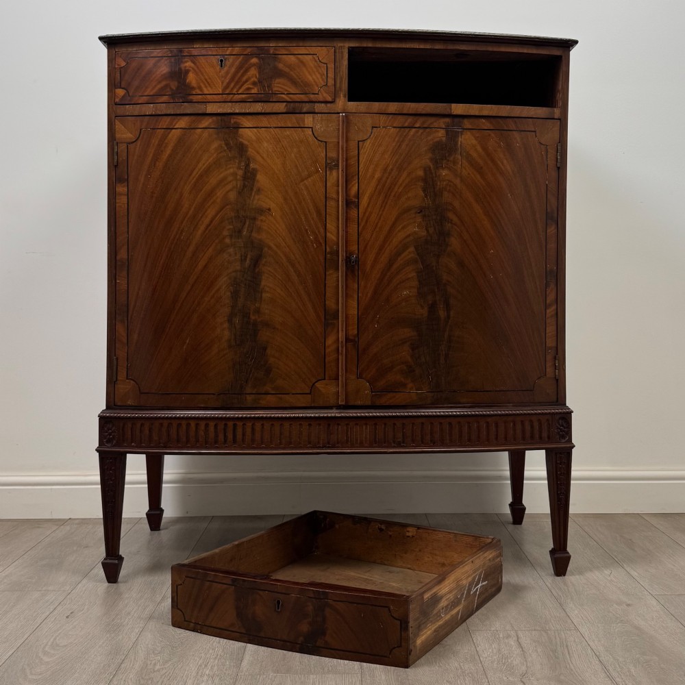 An 18th-century Georgian mahogany cupboard featuring flame veneer panelled doors, upper drawer section, a fluted apron, and tapered legs. View XI