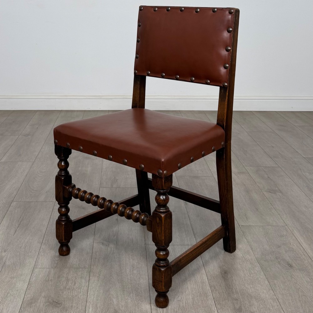 A set of eight dark oak dining chairs featuring brown leather upholstery secured with brass studding, turned legs, and including two armchairs. View III