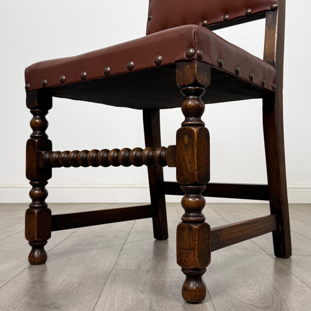 A set of eight dark oak dining chairs featuring brown leather upholstery secured with brass studding, turned legs, and including two armchairs. View VI