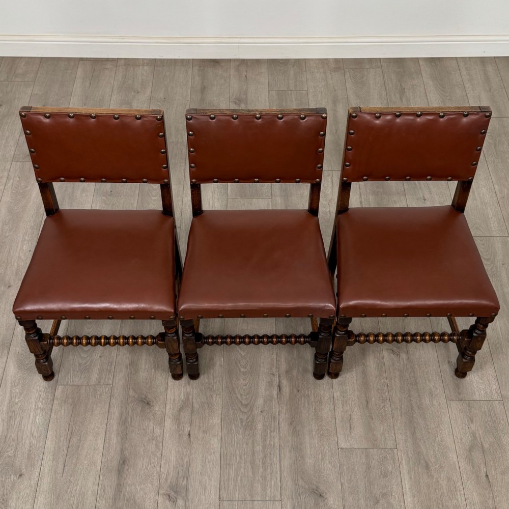 A set of eight dark oak dining chairs featuring brown leather upholstery secured with brass studding, turned legs, and including two armchairs. View IX