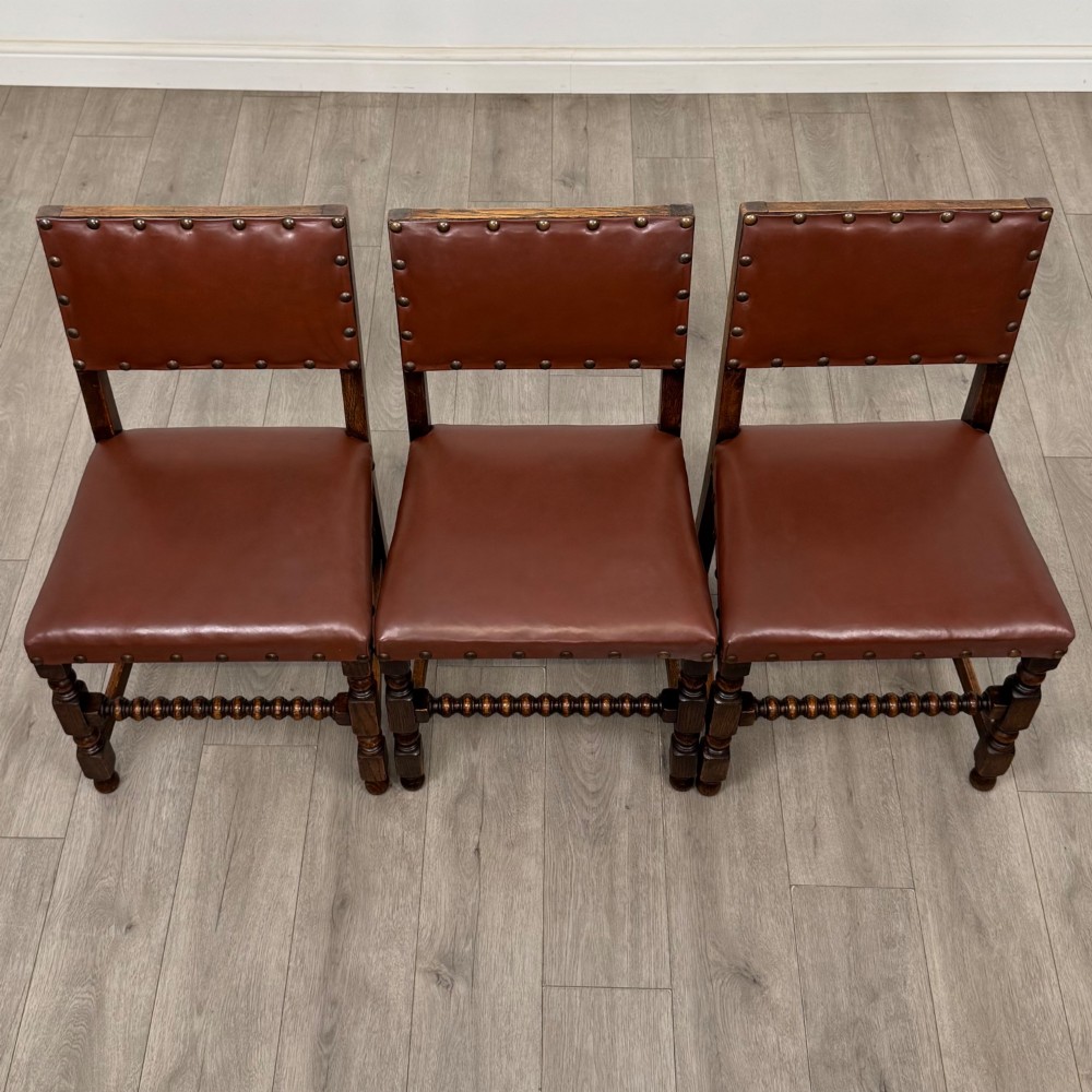 A set of eight dark oak dining chairs featuring brown leather upholstery secured with brass studding, turned legs, and including two armchairs. View X