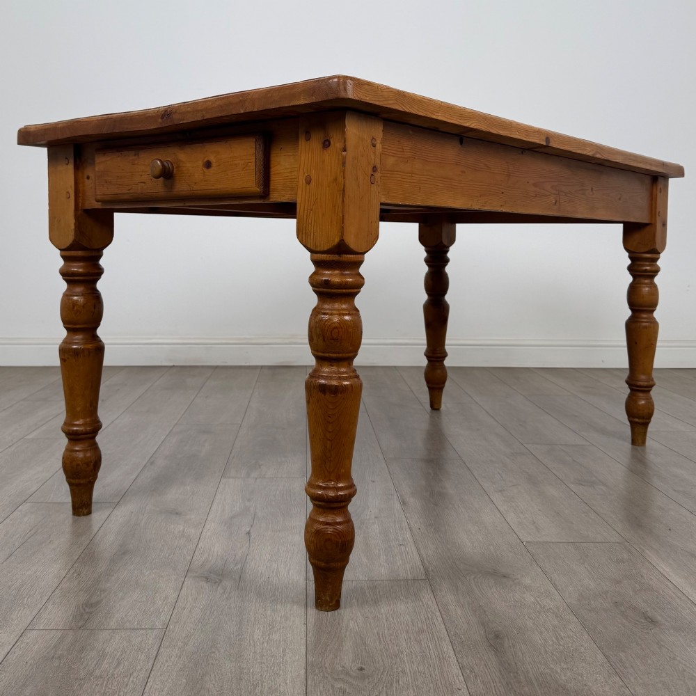 A solid pine farmhouse dining table featuring four turned legs and a single side frieze drawer with a wooden knob handle.