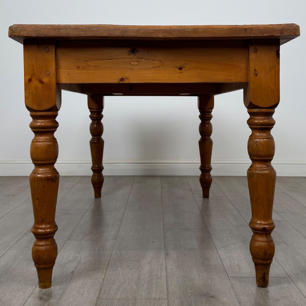 A solid pine farmhouse dining table featuring four turned legs and a single side frieze drawer with a wooden knob handle. View IV