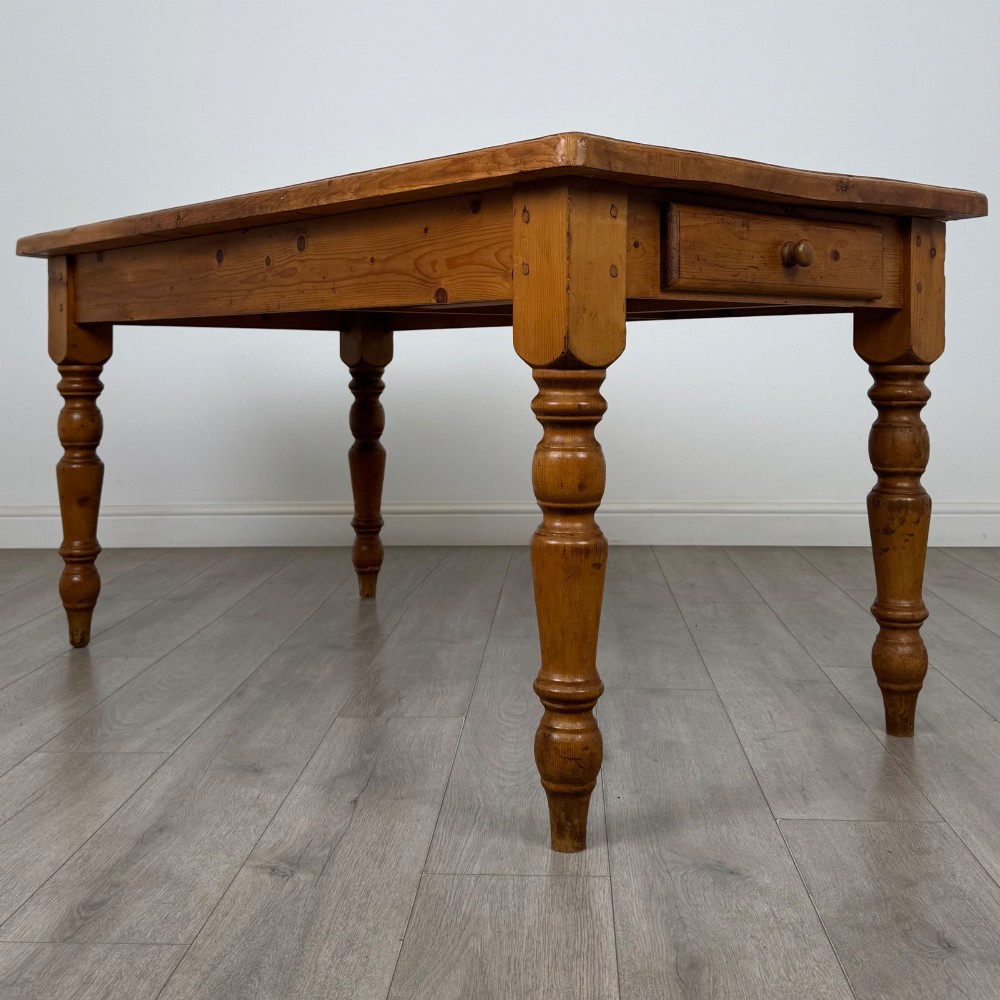 A solid pine farmhouse dining table featuring four turned legs and a single side frieze drawer with a wooden knob handle. View VII