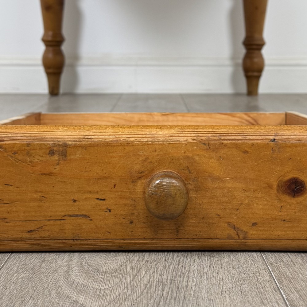 A solid pine farmhouse dining table featuring four turned legs and a single side frieze drawer with a wooden knob handle. View X
