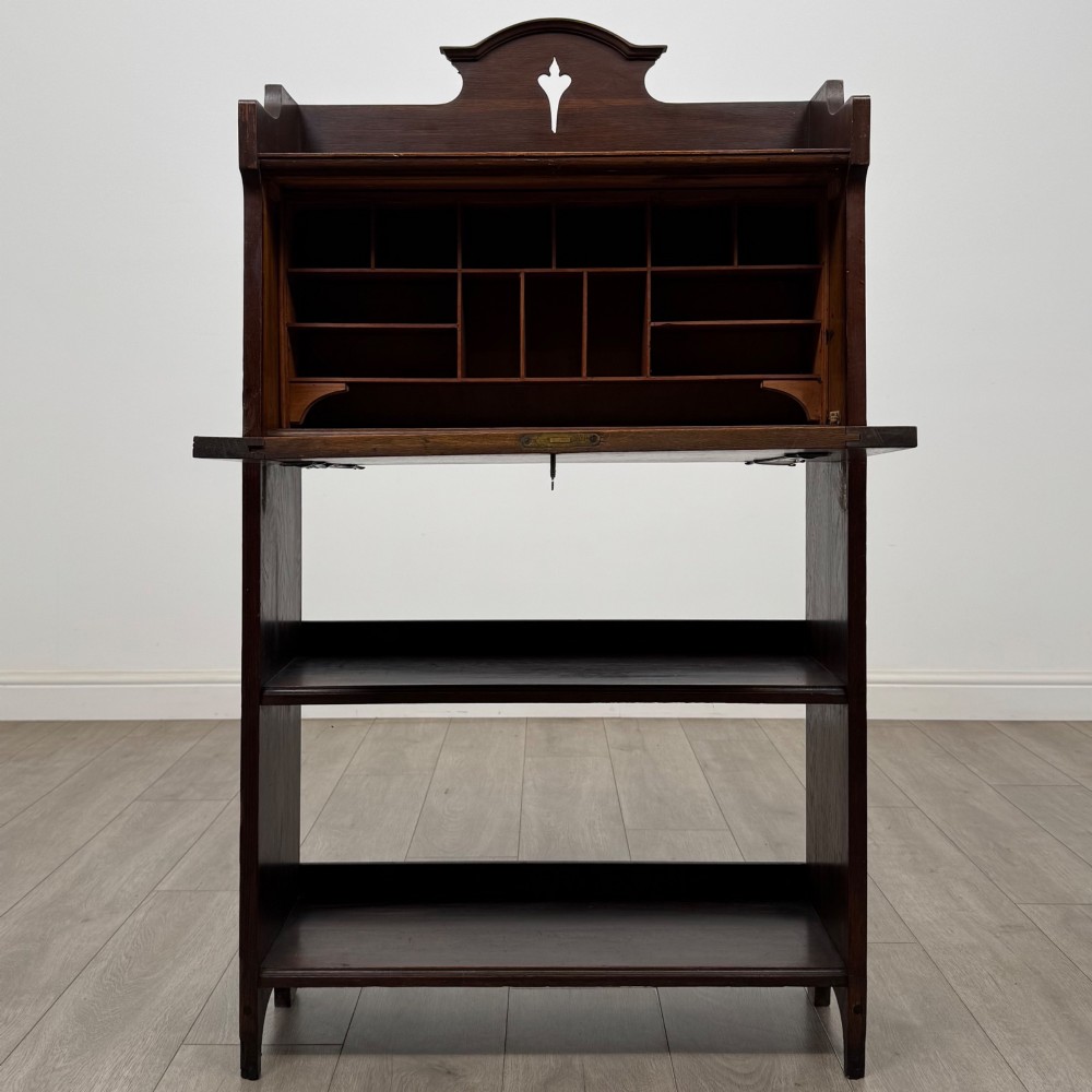 A dark mahogany Art Nouveau style bureau featuring a drop-front writing flap with elongated metal strap hinges above two open shelves. View III