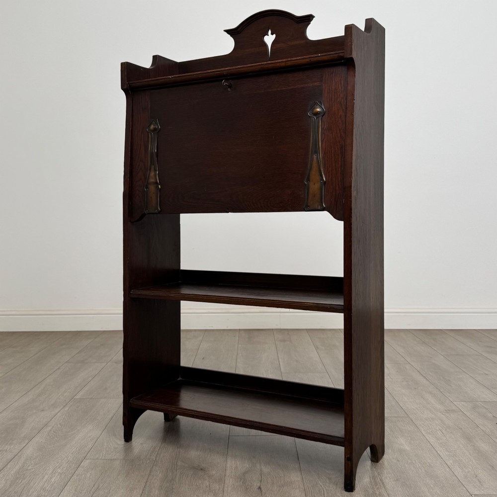A dark mahogany Art Nouveau style bureau featuring a drop-front writing flap with elongated metal strap hinges above two open shelves. View IV