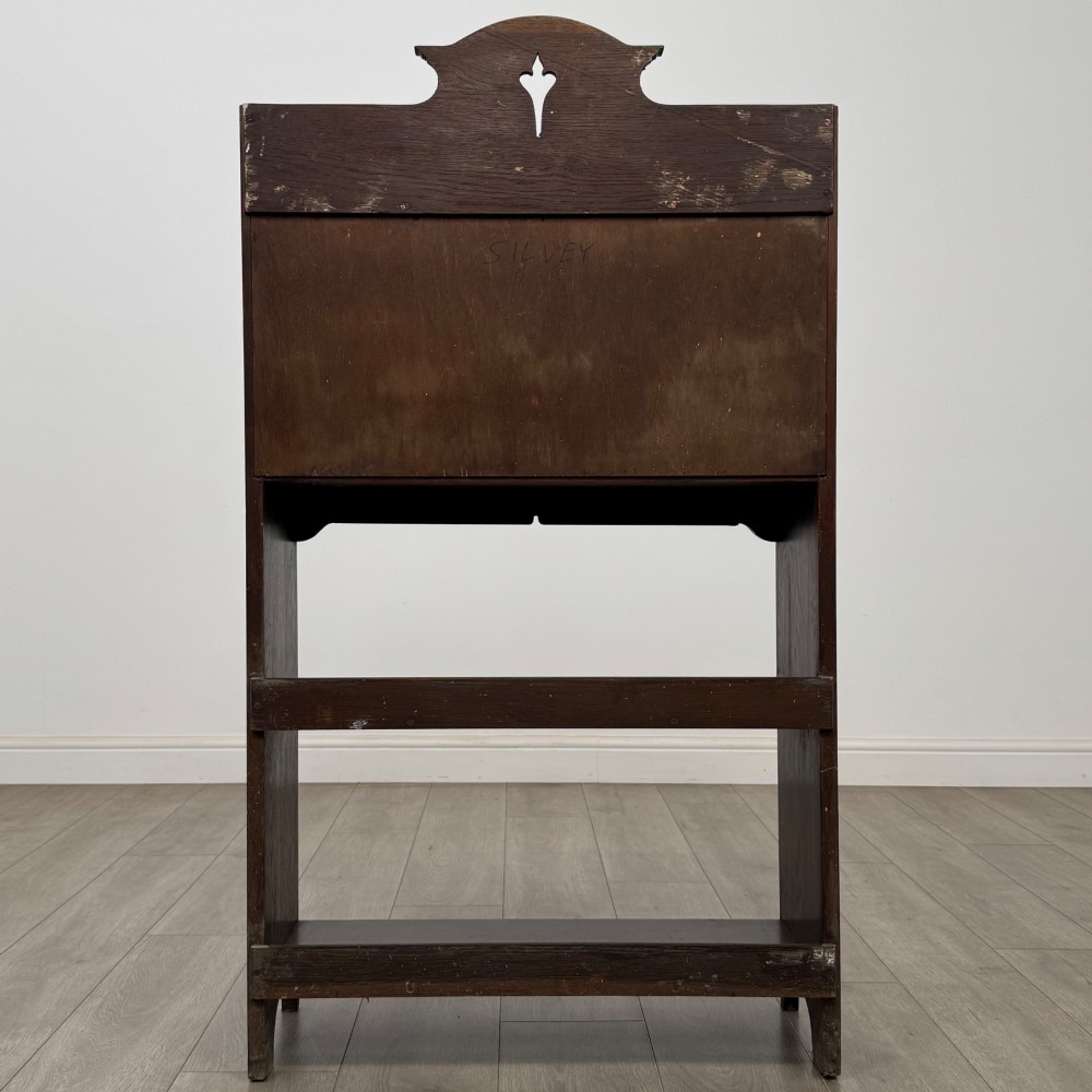 A dark mahogany Art Nouveau style bureau featuring a drop-front writing flap with elongated metal strap hinges above two open shelves. View VII