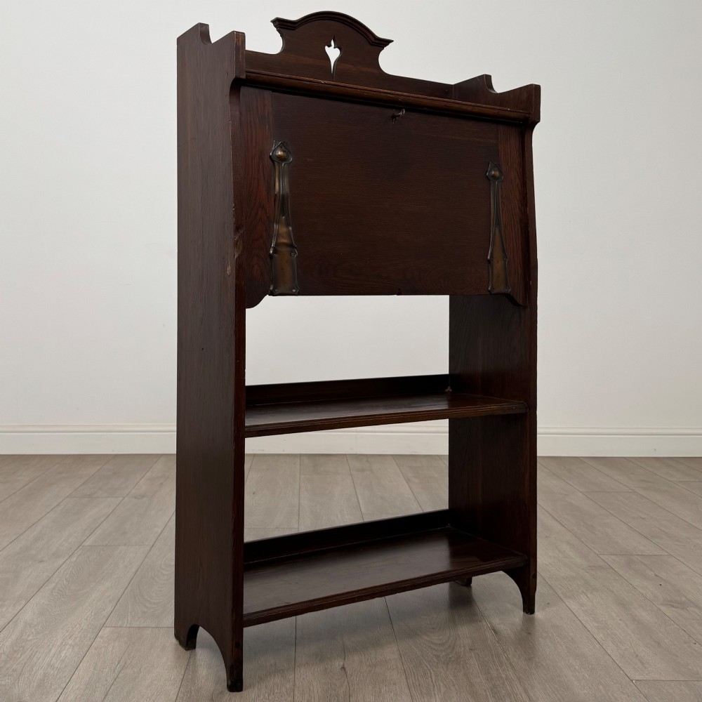 A dark mahogany Art Nouveau style bureau featuring a drop-front writing flap with elongated metal strap hinges above two open shelves. View X
