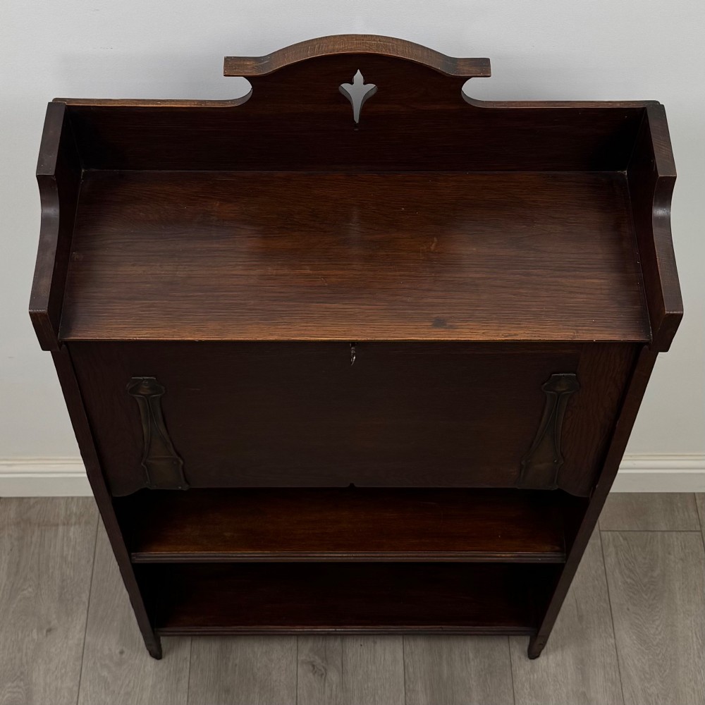 A dark mahogany Art Nouveau style bureau featuring a drop-front writing flap with elongated metal strap hinges above two open shelves. View XI