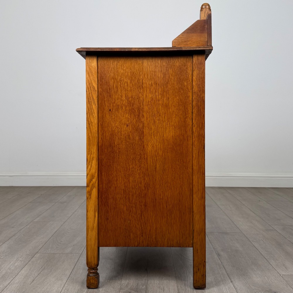 An antique Edwardian oak chest featuring three full-width drawers with dark metal drop handles and a shaped gallery back with turned finials. View III