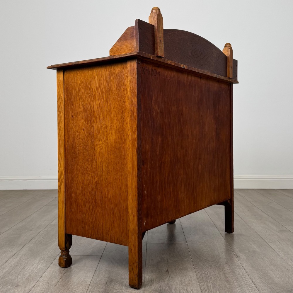 An antique Edwardian oak chest featuring three full-width drawers with dark metal drop handles and a shaped gallery back with turned finials. View IV