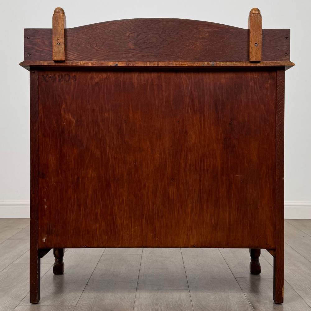 An antique Edwardian oak chest featuring three full-width drawers with dark metal drop handles and a shaped gallery back with turned finials. View V