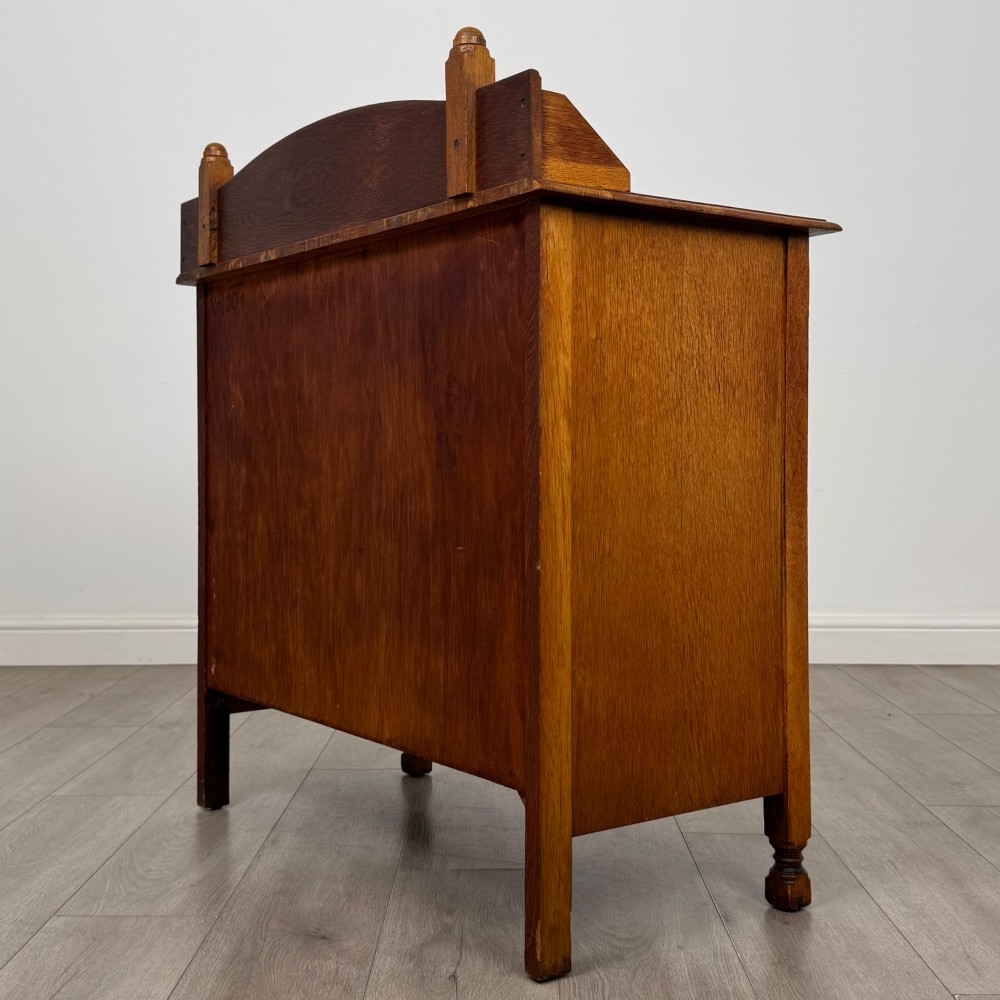 An antique Edwardian oak chest featuring three full-width drawers with dark metal drop handles and a shaped gallery back with turned finials. View VI