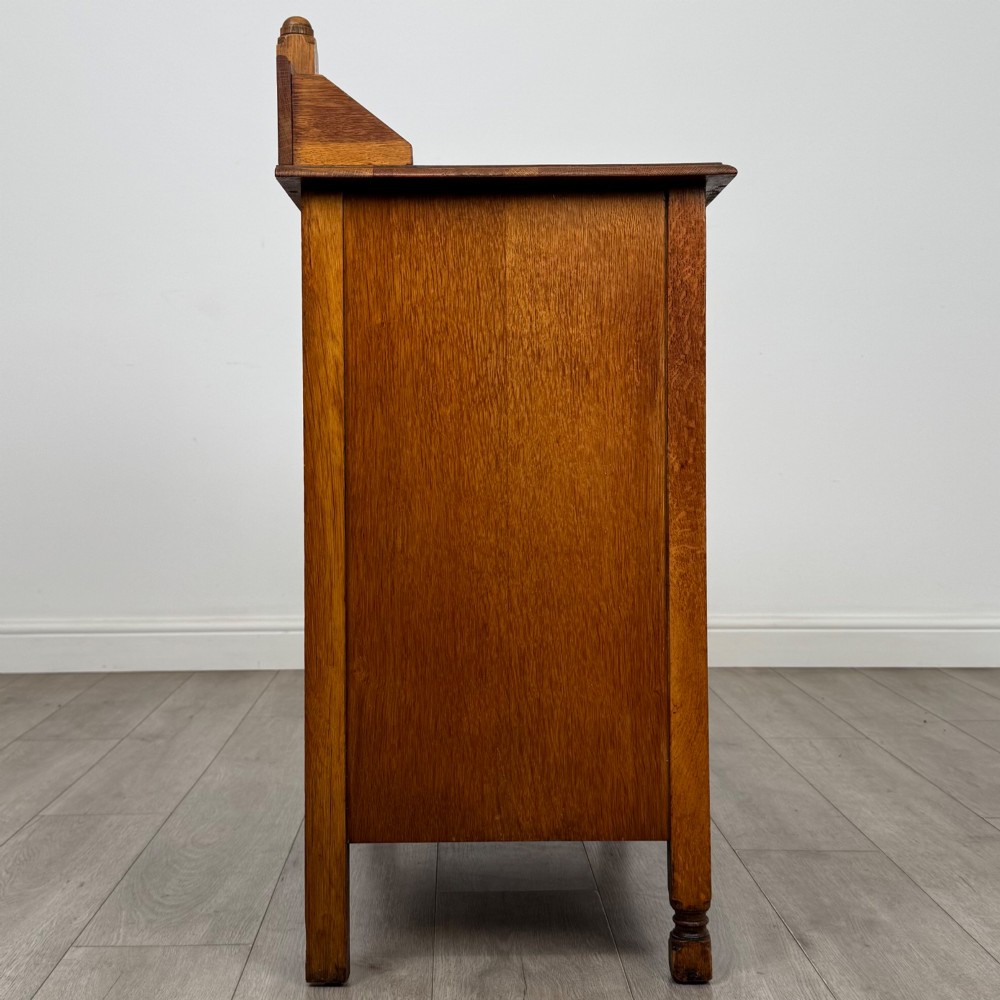 An antique Edwardian oak chest featuring three full-width drawers with dark metal drop handles and a shaped gallery back with turned finials. View VII