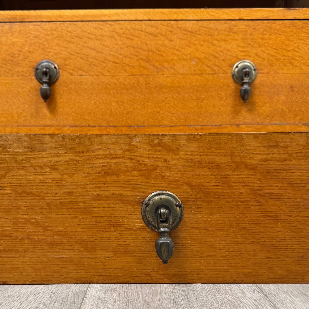 An antique Edwardian oak chest featuring three full-width drawers with dark metal drop handles and a shaped gallery back with turned finials. View XI