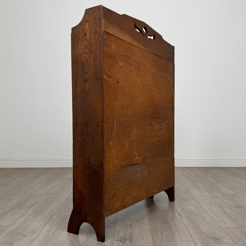 An early 20th-century Arts and Crafts medium oak open bookcase featuring four fixed shelves and a pierced stylised heart motif cut into the arched gallery top. View V