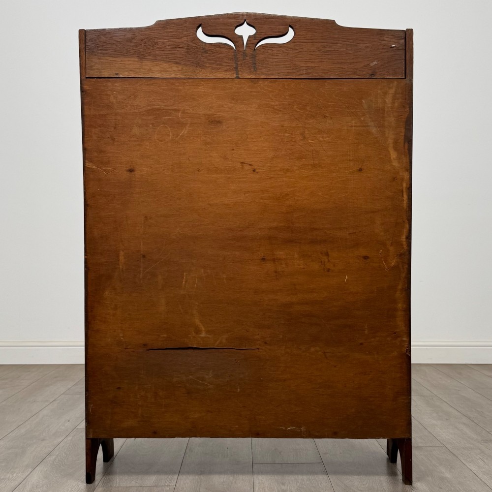 An early 20th-century Arts and Crafts medium oak open bookcase featuring four fixed shelves and a pierced stylised heart motif cut into the arched gallery top. View VI