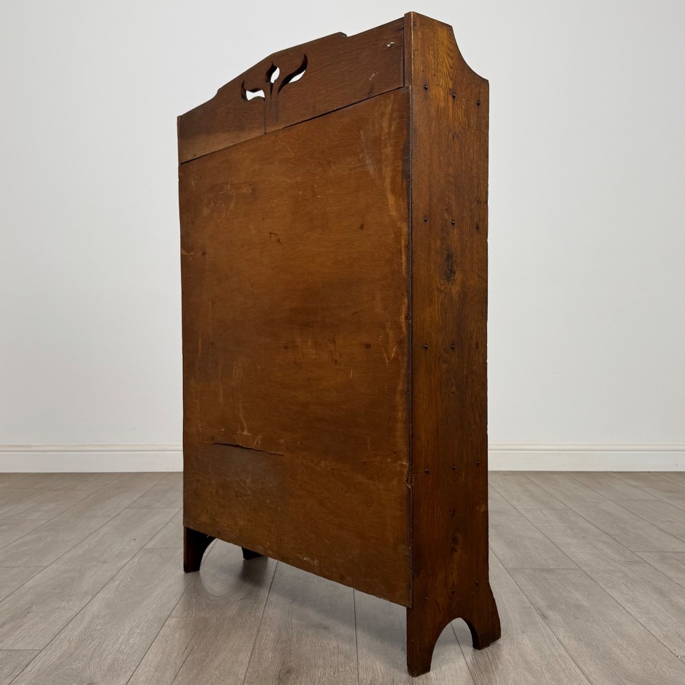 An early 20th-century Arts and Crafts medium oak open bookcase featuring four fixed shelves and a pierced stylised heart motif cut into the arched gallery top. View VII