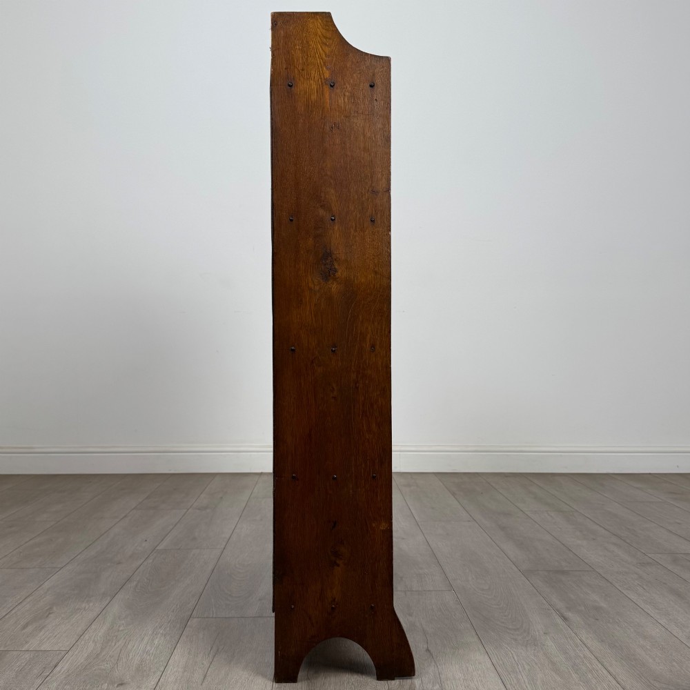 An early 20th-century Arts and Crafts medium oak open bookcase featuring four fixed shelves and a pierced stylised heart motif cut into the arched gallery top. View VIII