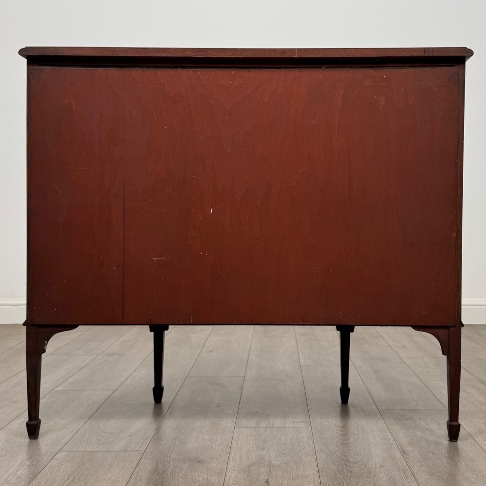 An Edwardian mahogany display cabinet featuring a central glazed door with curved glazing bars, flanked by curved side panels with inlaid floral motifs, raised on tapered legs. View VI