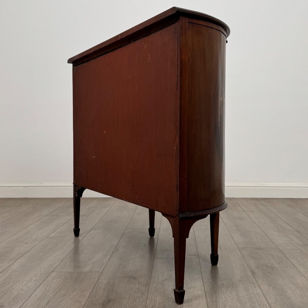An Edwardian mahogany display cabinet featuring a central glazed door with curved glazing bars, flanked by curved side panels with inlaid floral motifs, raised on tapered legs. View VII