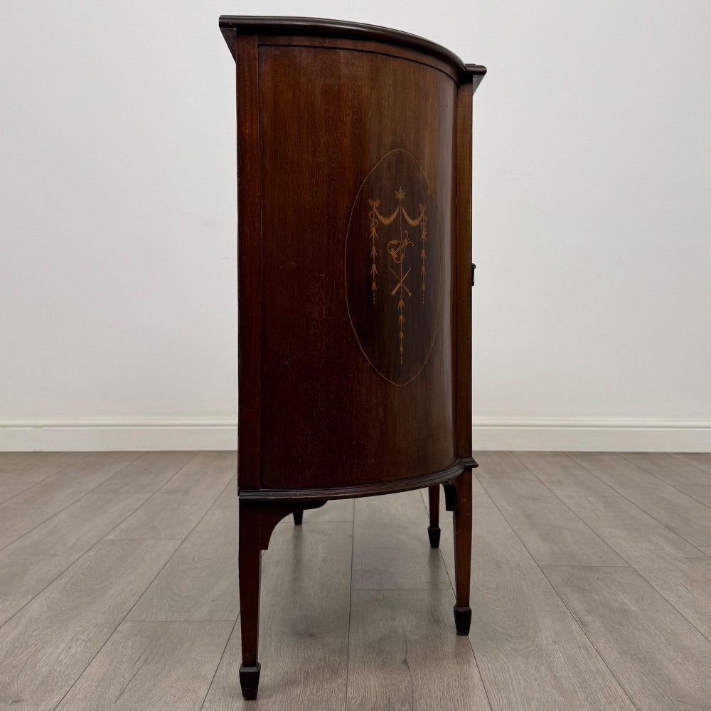 An Edwardian mahogany display cabinet featuring a central glazed door with curved glazing bars, flanked by curved side panels with inlaid floral motifs, raised on tapered legs. View VIII