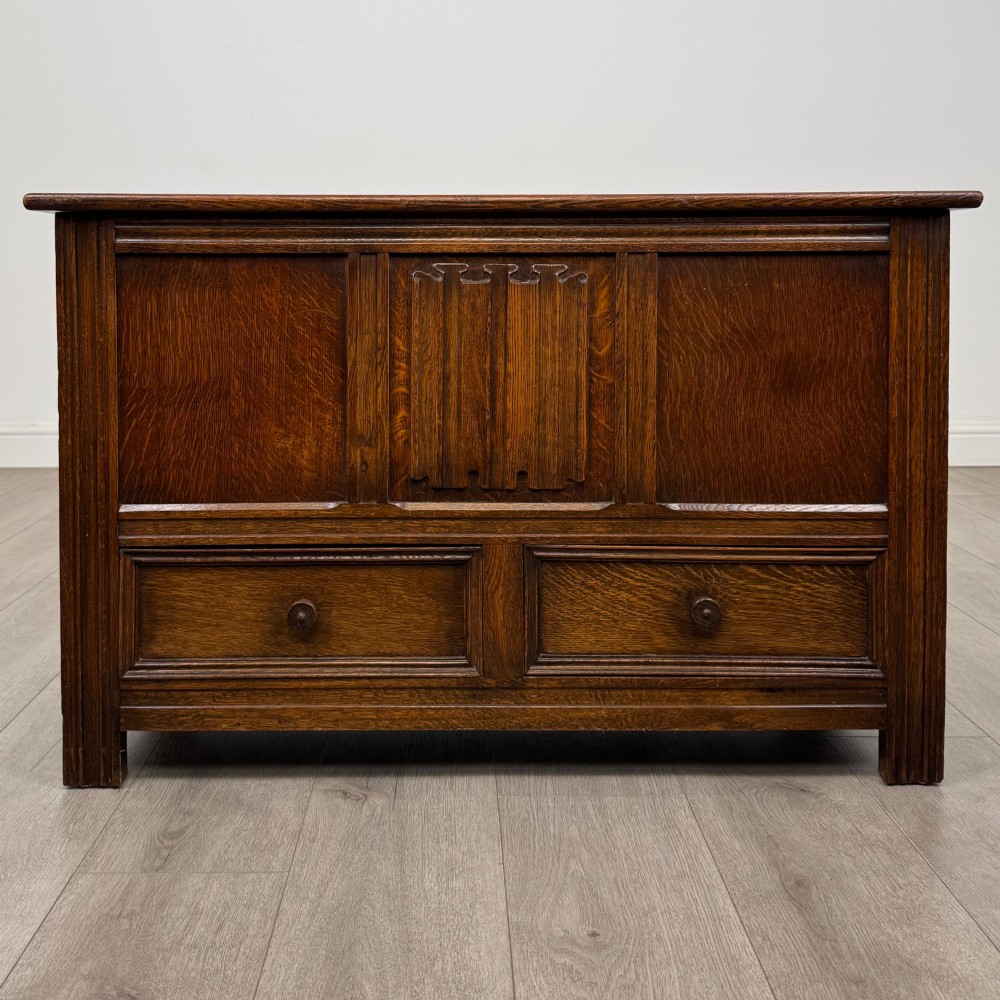An Edwardian oak mule chest with a panelled front, central carved detailing, and two bottom drawers with turned wooden knobs.