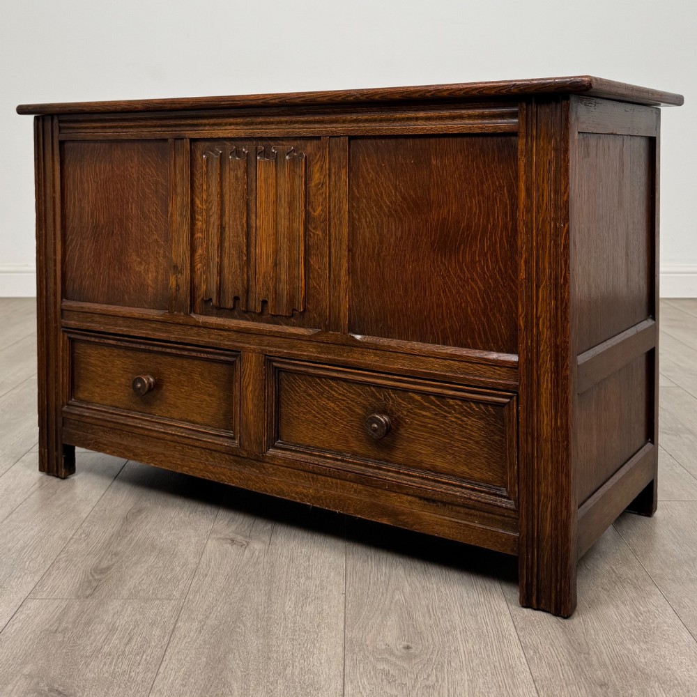 An Edwardian oak mule chest with a panelled front, central carved detailing, and two bottom drawers with turned wooden knobs. View II