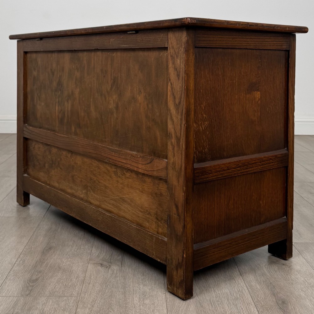An Edwardian oak mule chest with a panelled front, central carved detailing, and two bottom drawers with turned wooden knobs. View VI