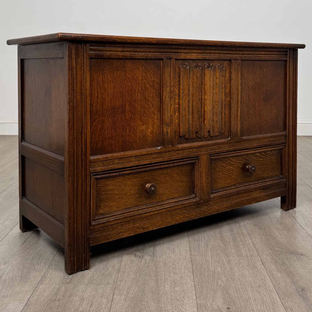 An Edwardian oak mule chest with a panelled front, central carved detailing, and two bottom drawers with turned wooden knobs. View VIII