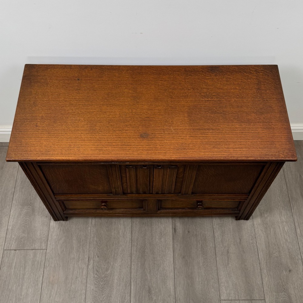 An Edwardian oak mule chest with a panelled front, central carved detailing, and two bottom drawers with turned wooden knobs. View IX