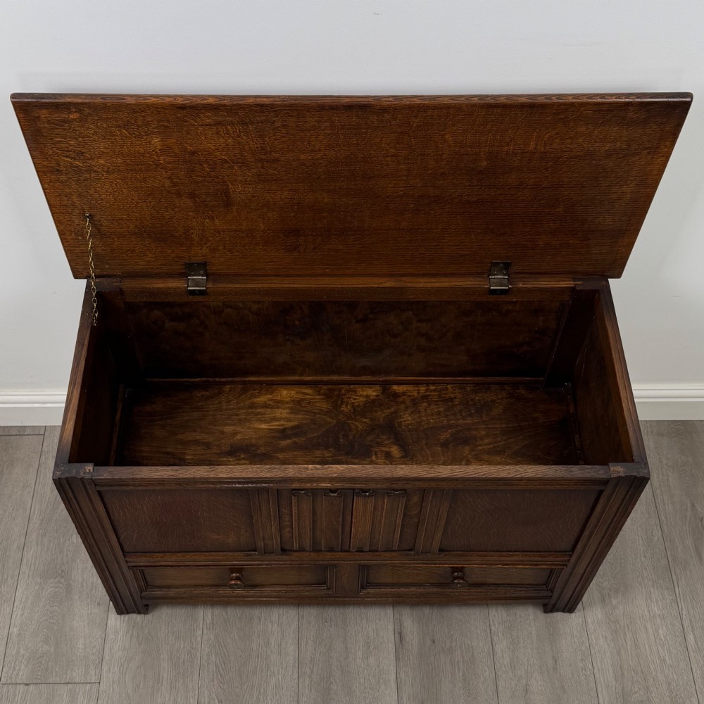 An Edwardian oak mule chest with a panelled front, central carved detailing, and two bottom drawers with turned wooden knobs. View X