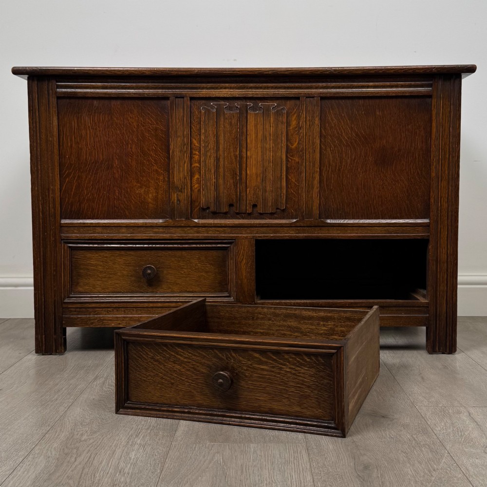 An Edwardian oak mule chest with a panelled front, central carved detailing, and two bottom drawers with turned wooden knobs. View XI