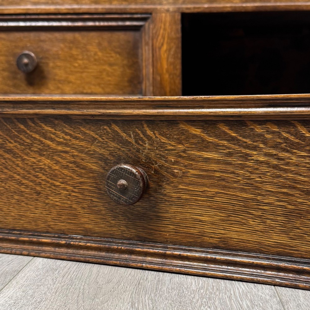 An Edwardian oak mule chest with a panelled front, central carved detailing, and two bottom drawers with turned wooden knobs. View XII