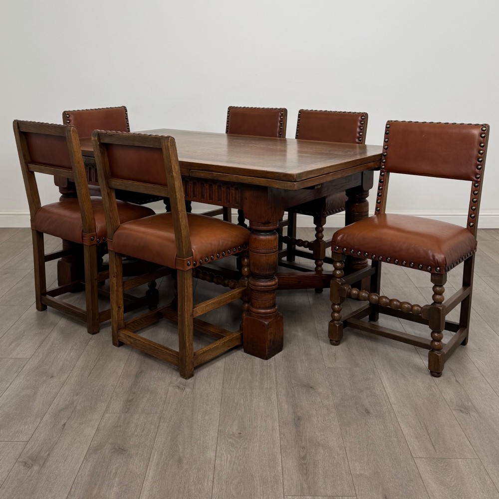 An antique oak dining table surrounded by six matching brown leather upholstered chairs with brass stud details.