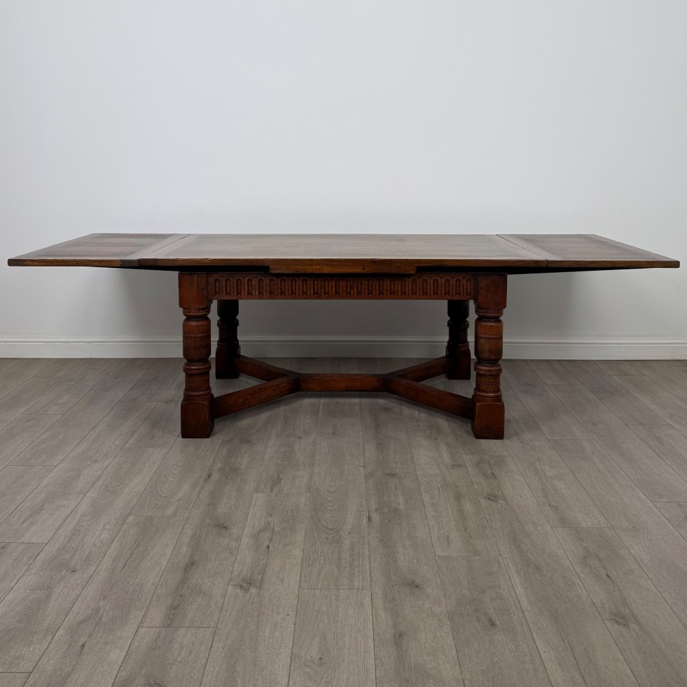 An antique oak dining table surrounded by six matching brown leather upholstered chairs with brass stud details. View II