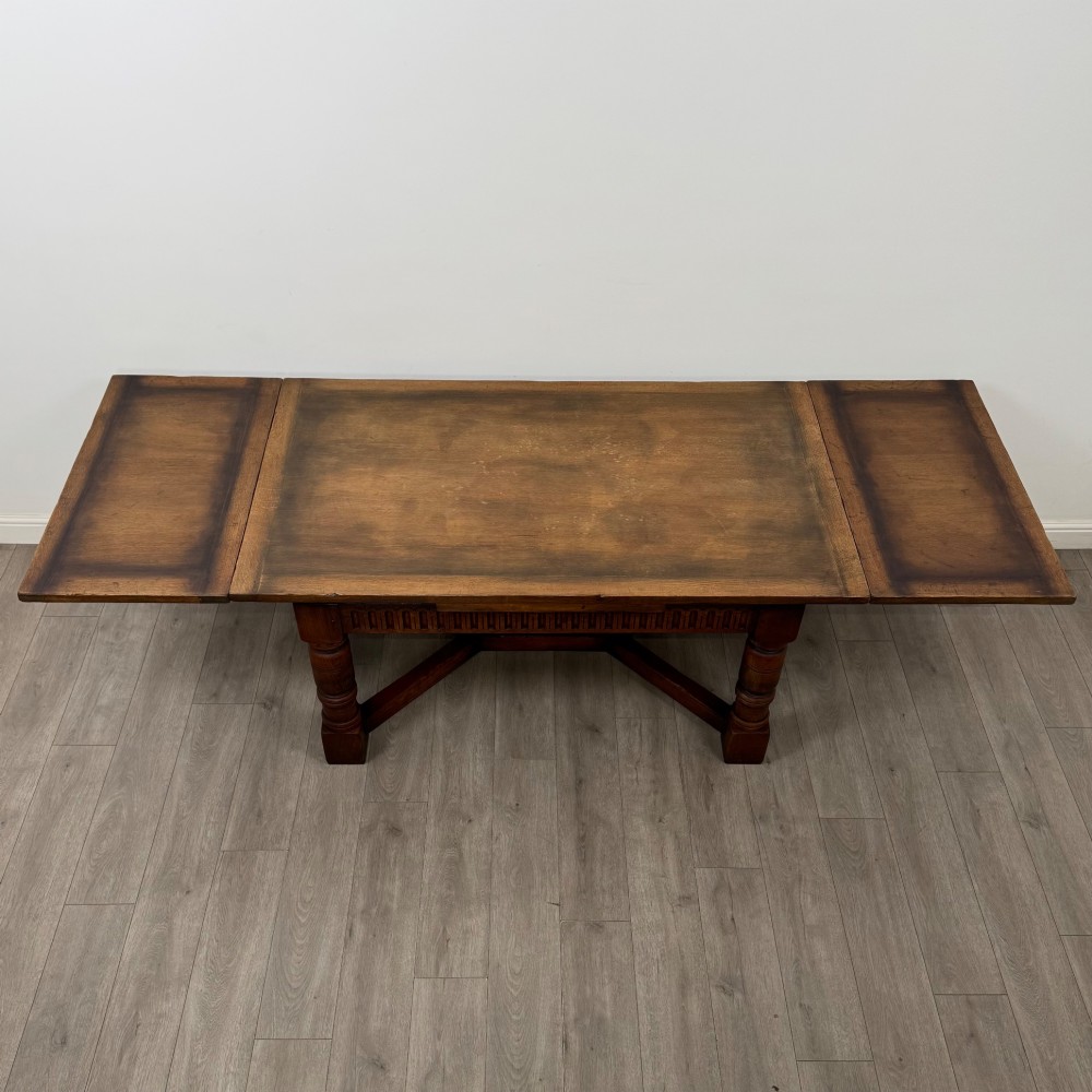 An antique oak dining table surrounded by six matching brown leather upholstered chairs with brass stud details. View V