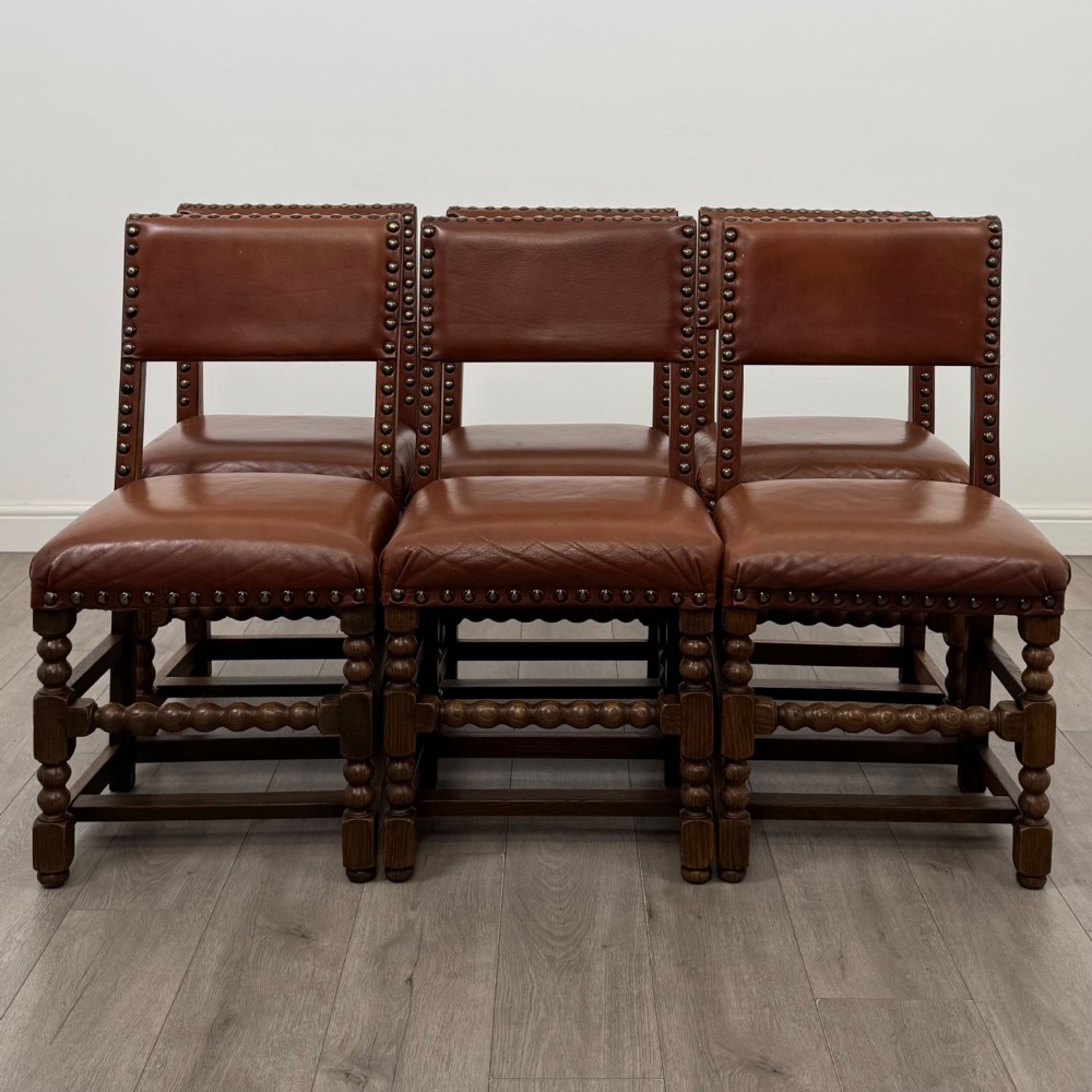 An antique oak dining table surrounded by six matching brown leather upholstered chairs with brass stud details. View VIII