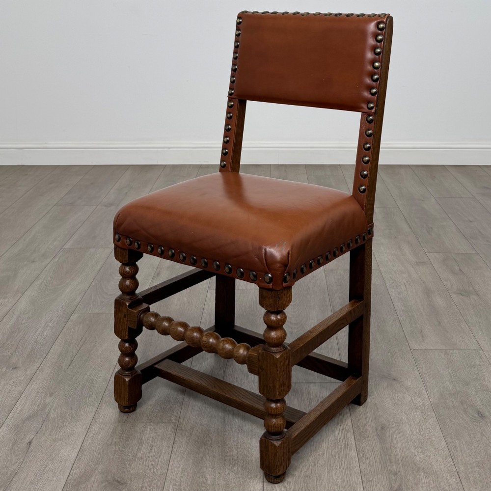 An antique oak dining table surrounded by six matching brown leather upholstered chairs with brass stud details. View IX
