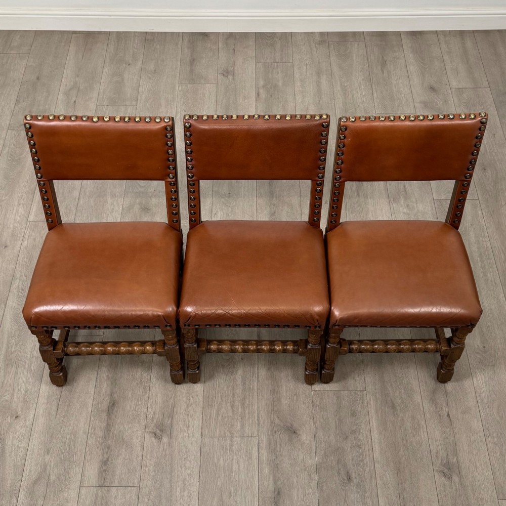 An antique oak dining table surrounded by six matching brown leather upholstered chairs with brass stud details. View XIV