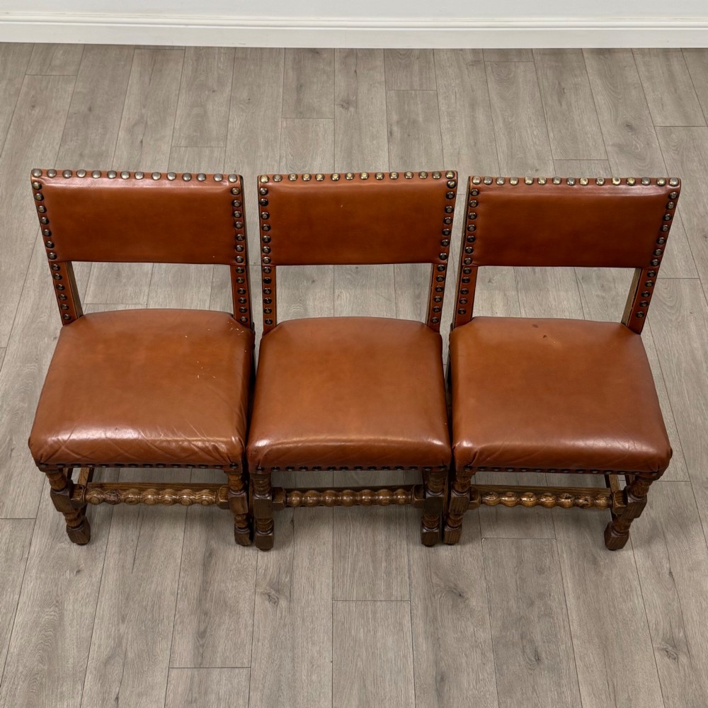 An antique oak dining table surrounded by six matching brown leather upholstered chairs with brass stud details. View XV