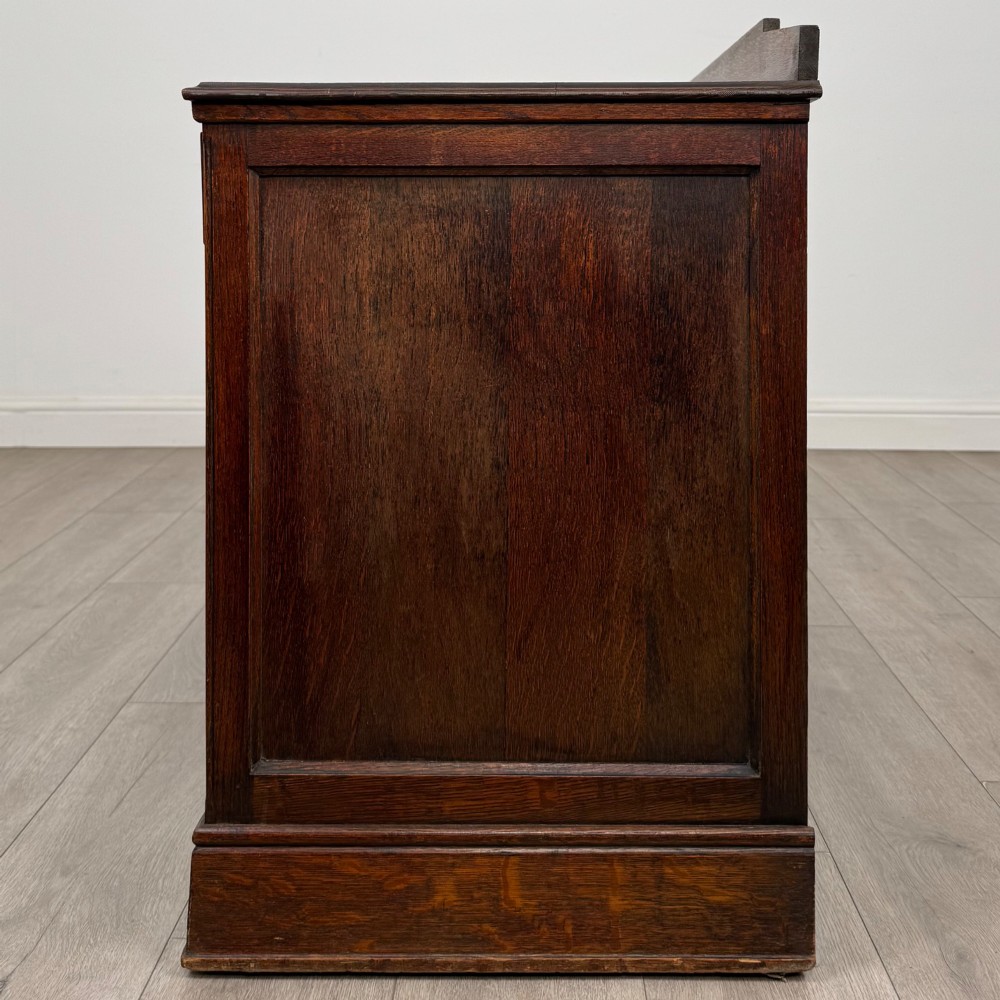 A dark carved oak Edwardian kneehole desk featuring frieze drawers with carved detailing and lower cupboard doors with vertical carved panels. View IV