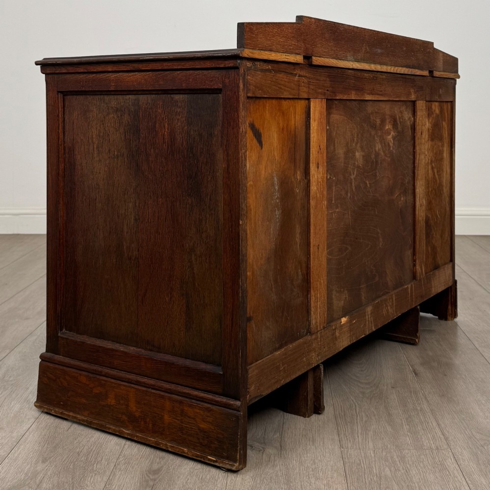 A dark carved oak Edwardian kneehole desk featuring frieze drawers with carved detailing and lower cupboard doors with vertical carved panels. View V