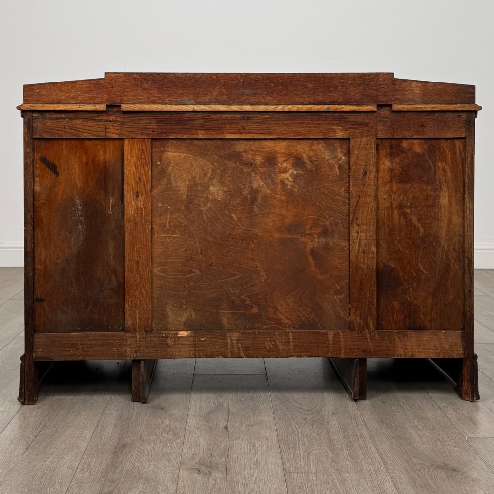 A dark carved oak Edwardian kneehole desk featuring frieze drawers with carved detailing and lower cupboard doors with vertical carved panels. View VI