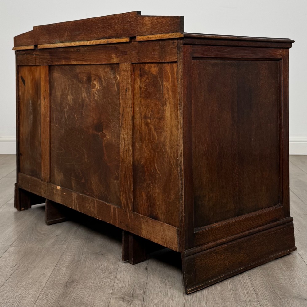 A dark carved oak Edwardian kneehole desk featuring frieze drawers with carved detailing and lower cupboard doors with vertical carved panels. View VII