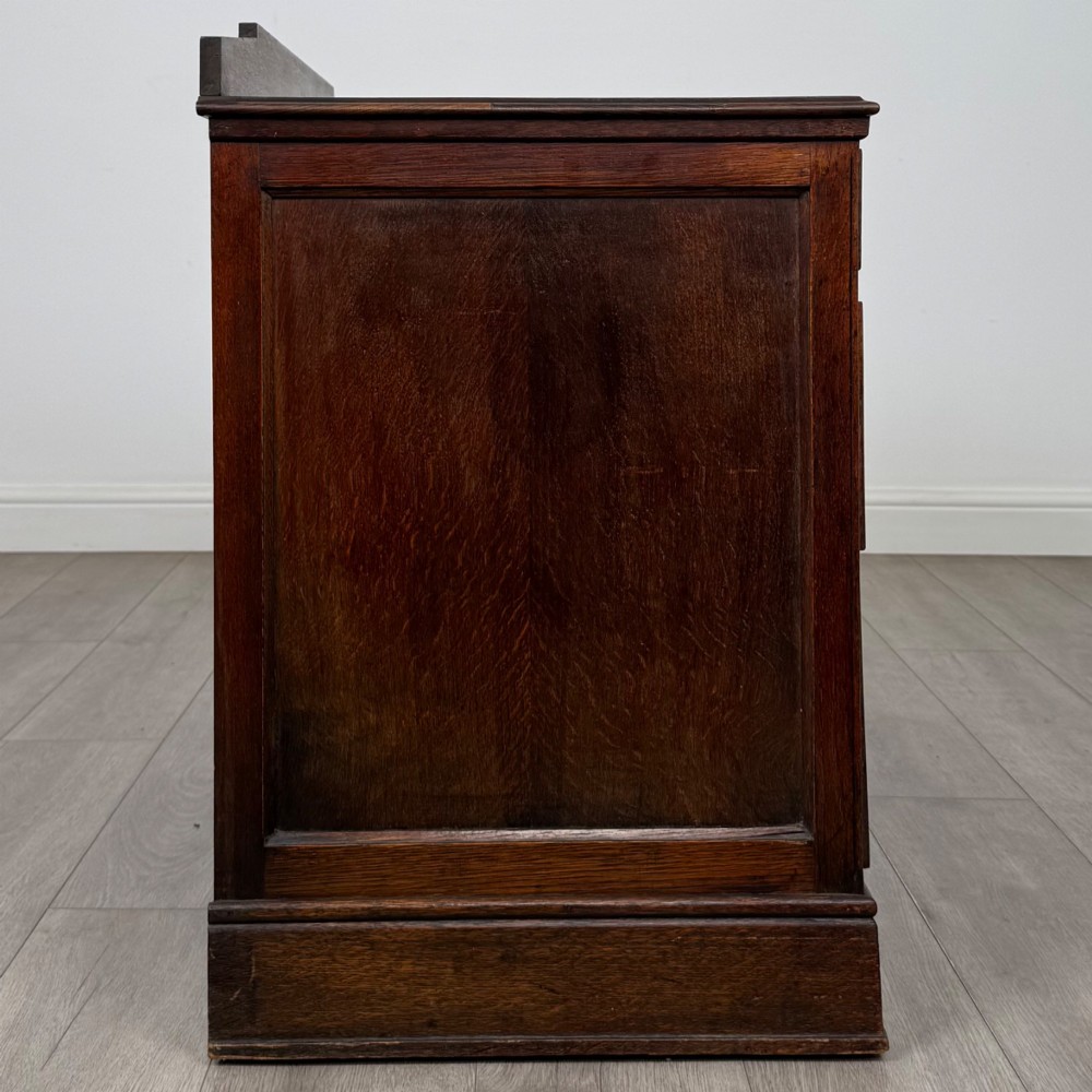 A dark carved oak Edwardian kneehole desk featuring frieze drawers with carved detailing and lower cupboard doors with vertical carved panels. View VIII