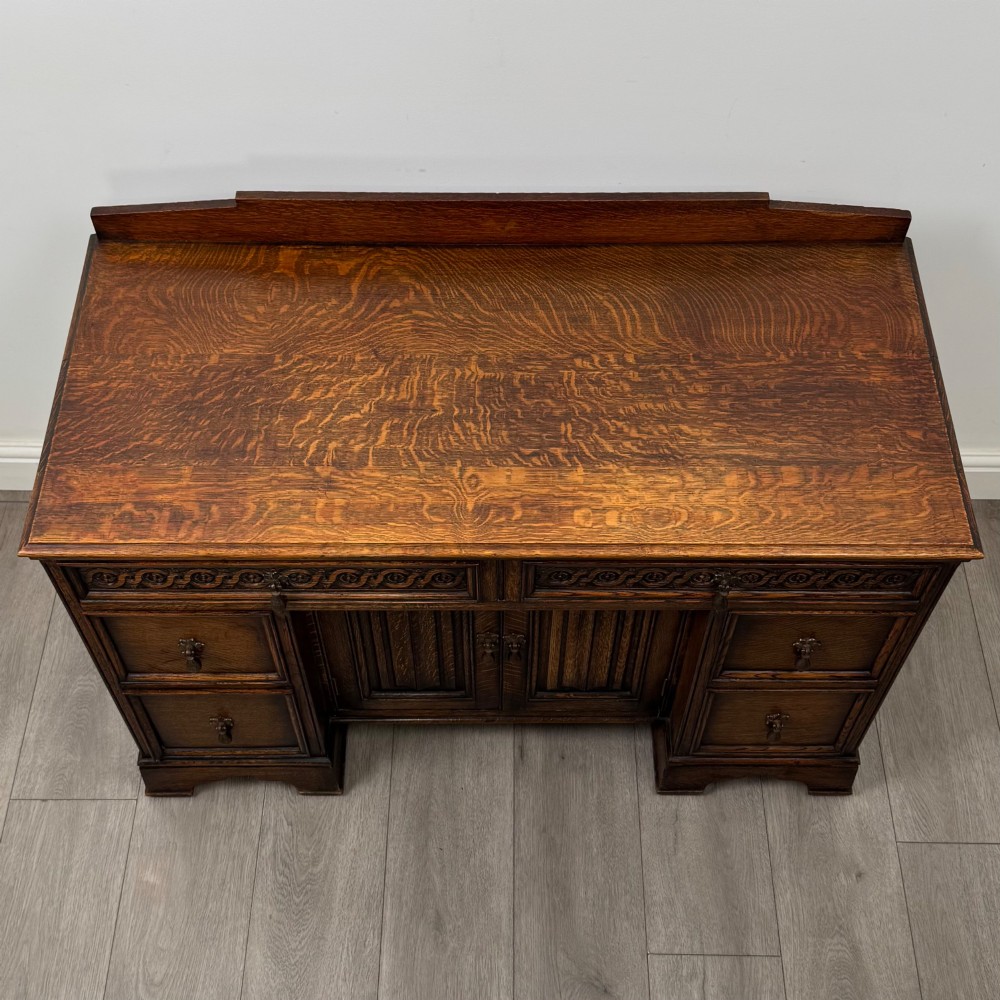 A dark carved oak Edwardian kneehole desk featuring frieze drawers with carved detailing and lower cupboard doors with vertical carved panels. View X