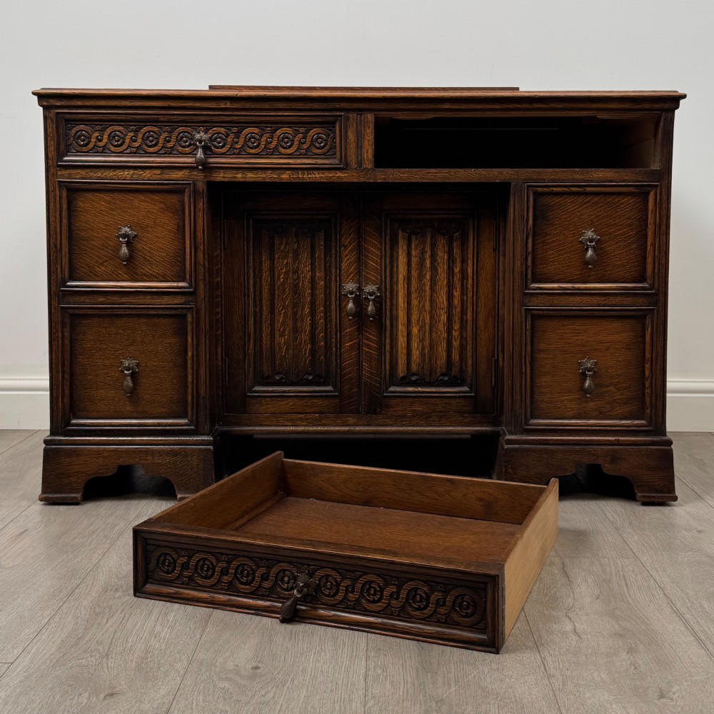 A dark carved oak Edwardian kneehole desk featuring frieze drawers with carved detailing and lower cupboard doors with vertical carved panels. View XI